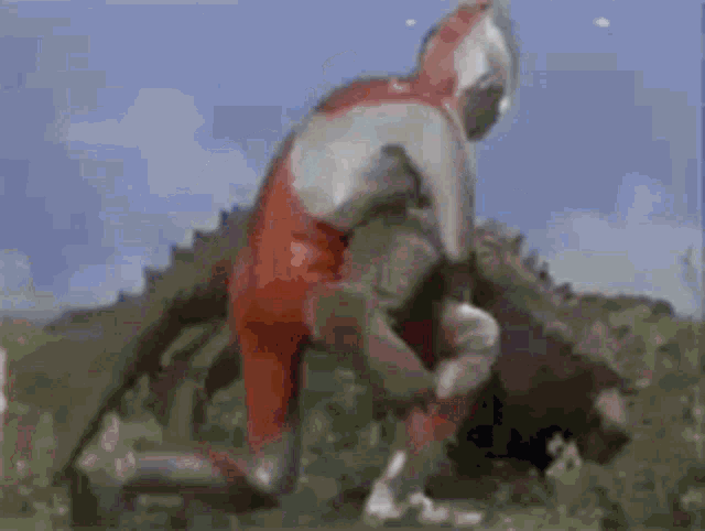 a man in a red and white suit is fighting a monster in a field .