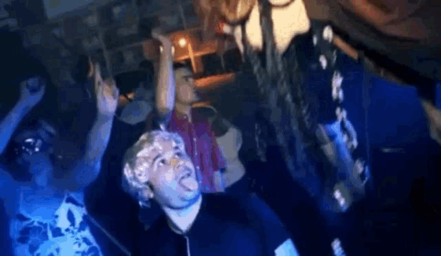 a group of people are dancing in a dark room and one of them is wearing a wig .