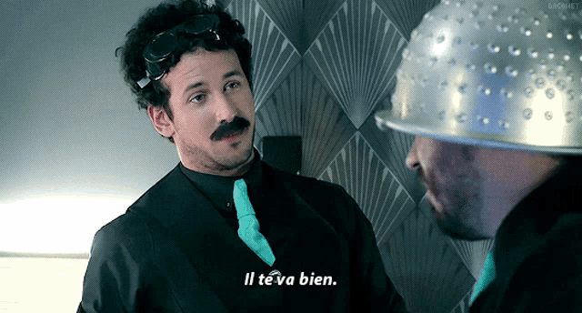 a man in a suit and tie says " il te va bien " to another man