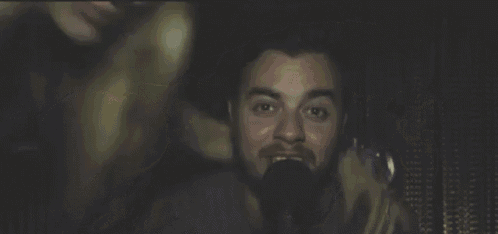 a man and a woman are sitting next to each other in a dark room . the woman has blonde hair and a beard .