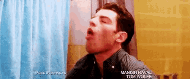 a man is yawning in front of a blue shower curtain in a bathroom .