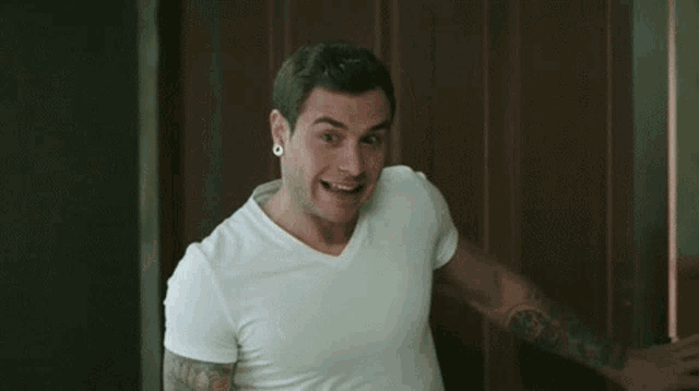a man in a white t-shirt is standing in a kitchen with his eyes closed and making a funny face .