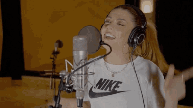 a woman singing into a microphone wearing headphones and a nike shirt
