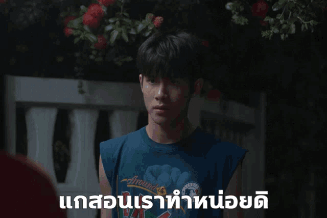 a young man wearing a blue sleeveless t-shirt is standing in front of a white fence in a dark room