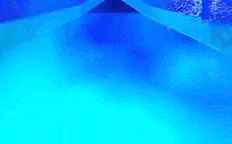 a blue water slide in a swimming pool with bubbles coming out of the water .