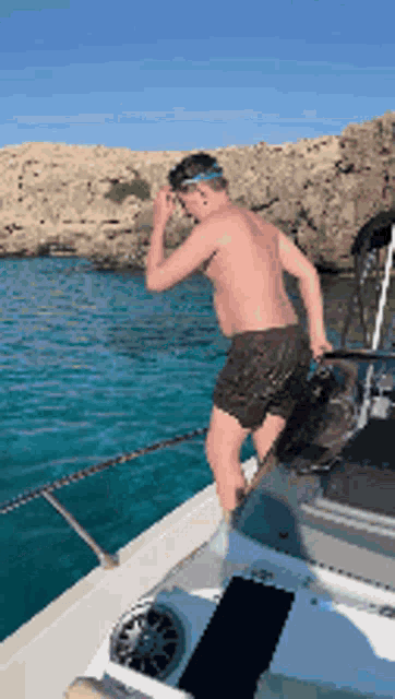 a shirtless man standing on the side of a boat in the water