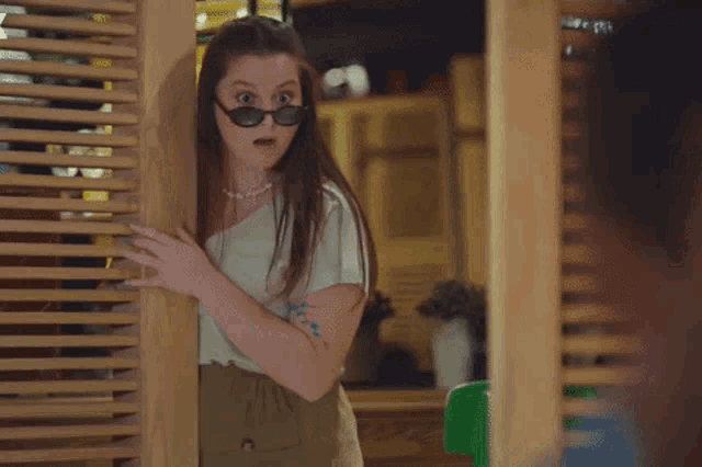 a woman wearing sunglasses is peeking out from behind a door .