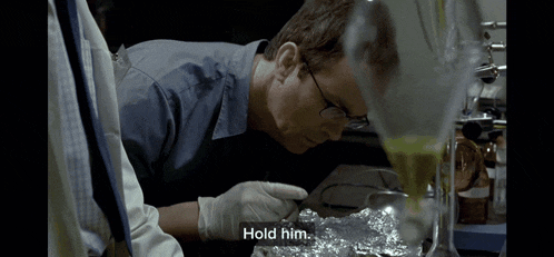 a man in a lab is being held by another man and says hold him