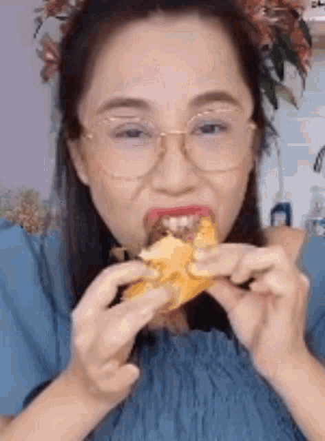 a woman wearing glasses is eating a sandwich with a flower in her hair .
