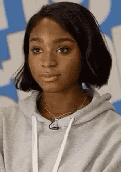 a close up of a woman wearing a gray hoodie and a necklace .