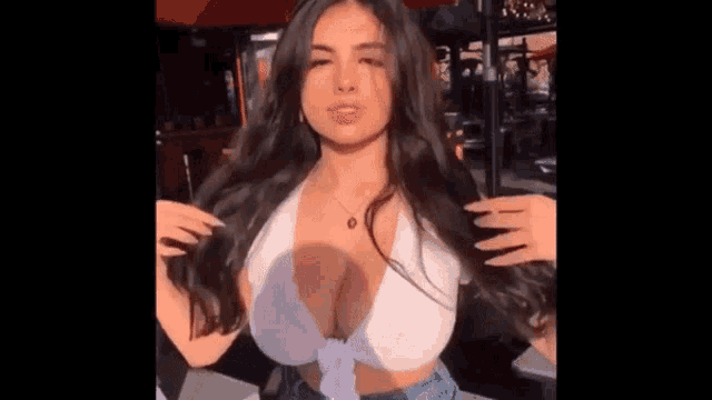 a woman with very large breasts is wearing a white crop top and blue shorts .