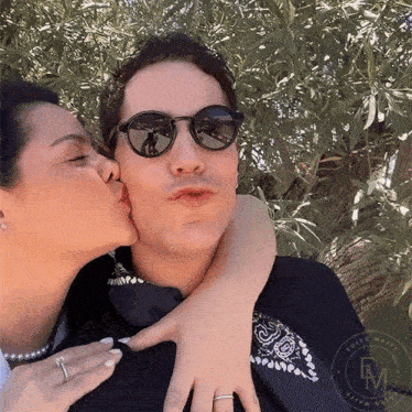 a woman kisses a man on the cheek while wearing sunglasses and a ring
