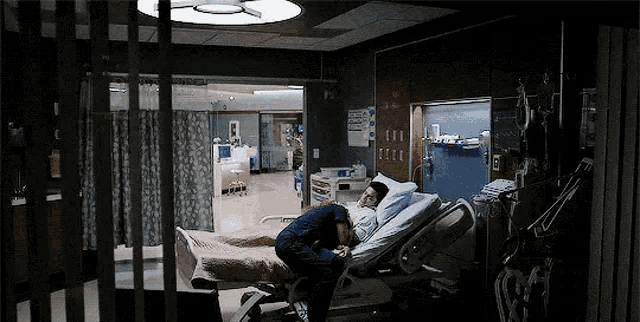 a man is kneeling over a patient in a hospital bed .