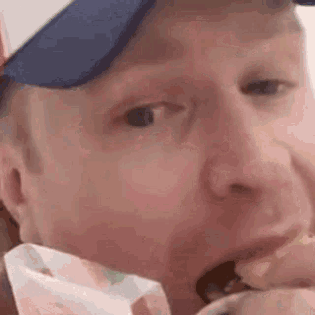 a man wearing a hat is eating a hamburger with his mouth open .
