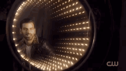 a man in a leather jacket is standing in a tunnel of lights with a cw logo on the bottom .