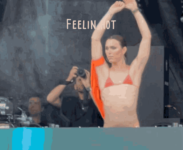 a woman in a bikini is dancing in front of a sign that says feeling hot