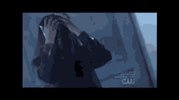 a woman with long hair is standing in a dark room with a cw logo on her shirt