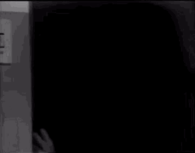 a black and white photo of a woman with long hair standing in a dark room .
