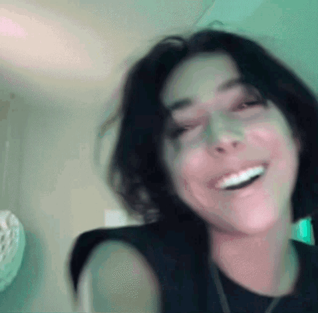 a woman wearing a black tank top and a necklace is smiling