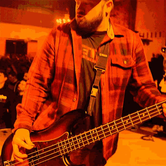 a man in a red plaid shirt is holding a bass guitar