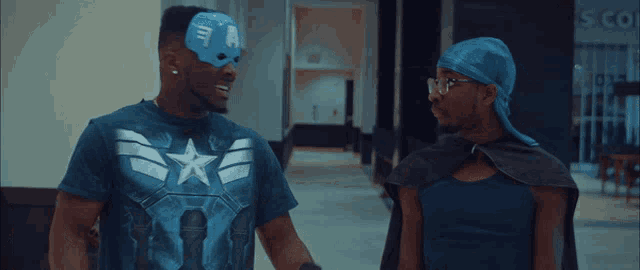 a man wearing a captain america mask stands next to another man in a cape