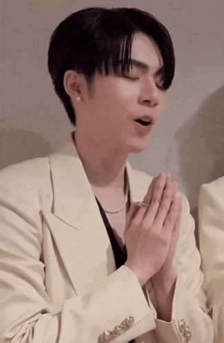 a man wearing a white jacket is praying with his hands together