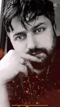 a man with a beard and a ring on his finger looks at the camera