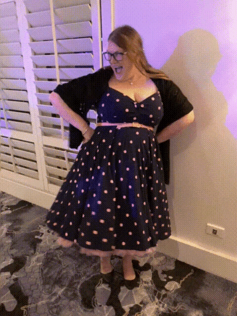 a woman in a polka dot dress is standing in front of a window