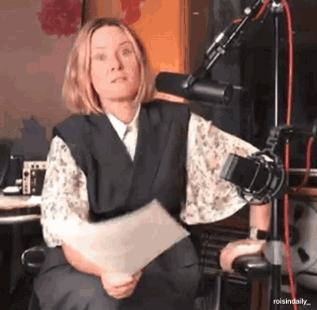 a woman is sitting in front of a microphone with a piece of paper in her hand .