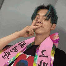a young man with blue hair is wearing a pink scarf around his neck and making a funny face .