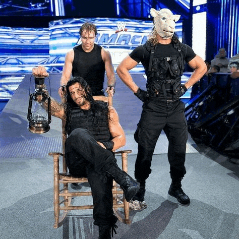a man in a sheep mask is sitting in a rocking chair while two men stand behind him .