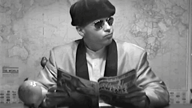a man wearing sunglasses and a hat is reading a magazine .