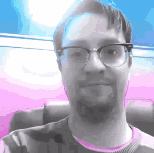 a man wearing glasses and a pink shirt is smiling