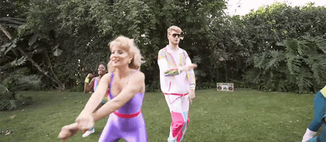 a man and a woman are dancing in a park with a boombox in the background