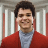 a young man in a red jacket is smiling for the camera .