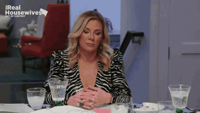a woman sits at a table with glasses of water in front of a sign that says real housewives