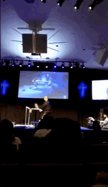a man stands on a stage in front of a large screen
