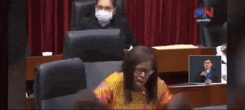 a woman in a floral dress is sitting in a chair in front of a sign language interpreter .