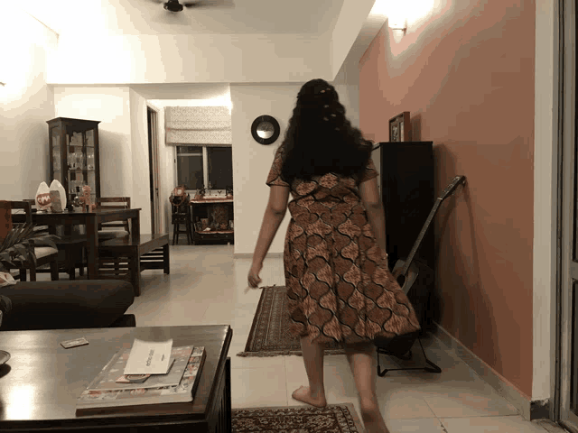 a woman in a dress is standing in a living room with a guitar in the background