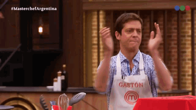 a man wearing an apron that says gaston is clapping his hands