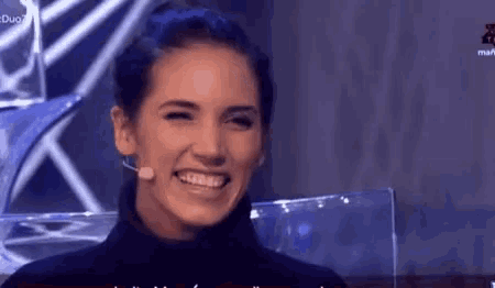 a woman is smiling while wearing a black turtleneck sweater and a microphone .
