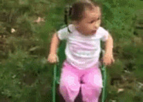 a little girl is sitting on a green chair in the grass .