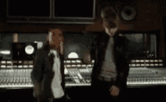 two men are standing next to each other in front of a sound board in a recording studio .