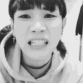a black and white photo of a young man wearing a hoodie and earrings making a funny face .