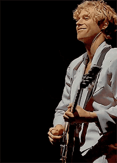 a man with blonde hair is playing a guitar on a stage