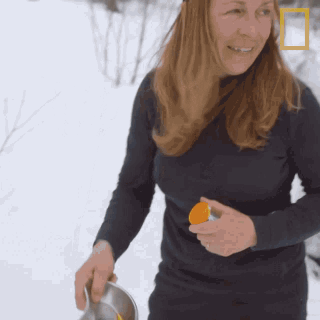 a woman in a black shirt is standing in the snow holding a container of orange juice