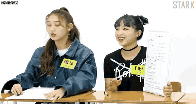 two girls sitting at a desk with one wearing a name tag that says cielo