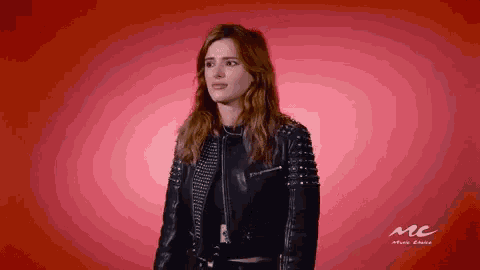 a woman wearing a black leather jacket with studs on the sleeves is standing in front of a red background .