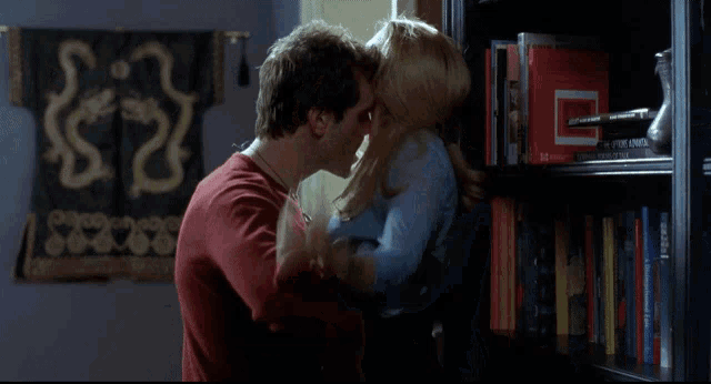 a man and a woman are hugging in front of a bookshelf with a red book titled " a brief history of the world "