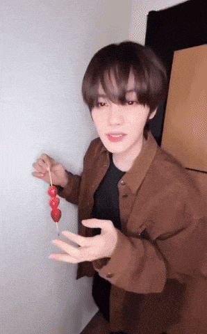 a young man in a brown jacket is holding a skewer with red berries on it